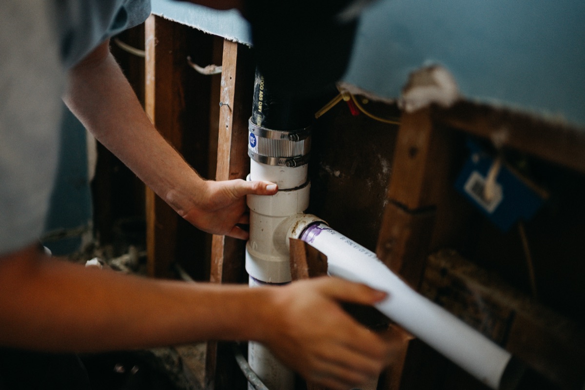 Close-up of hands fitting new PVC pipe between wall studs