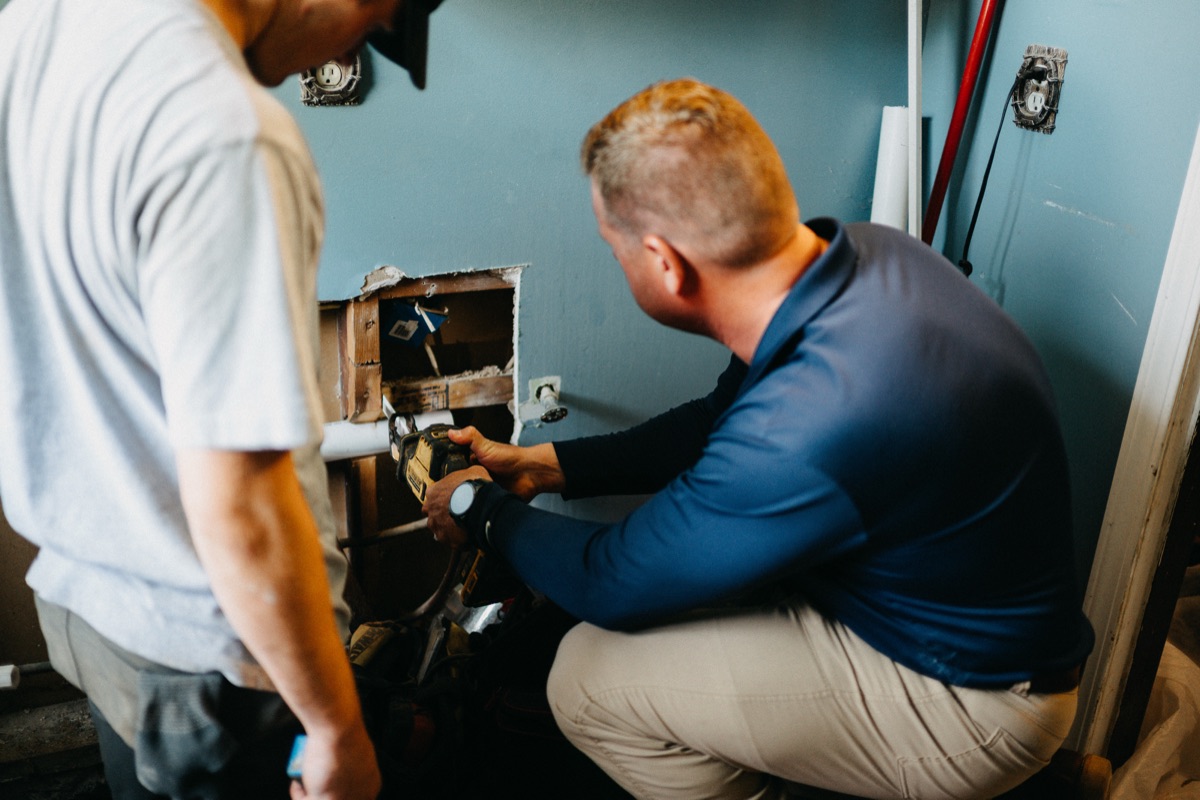 Two Matlock technicians repairing plumbing inside a wall